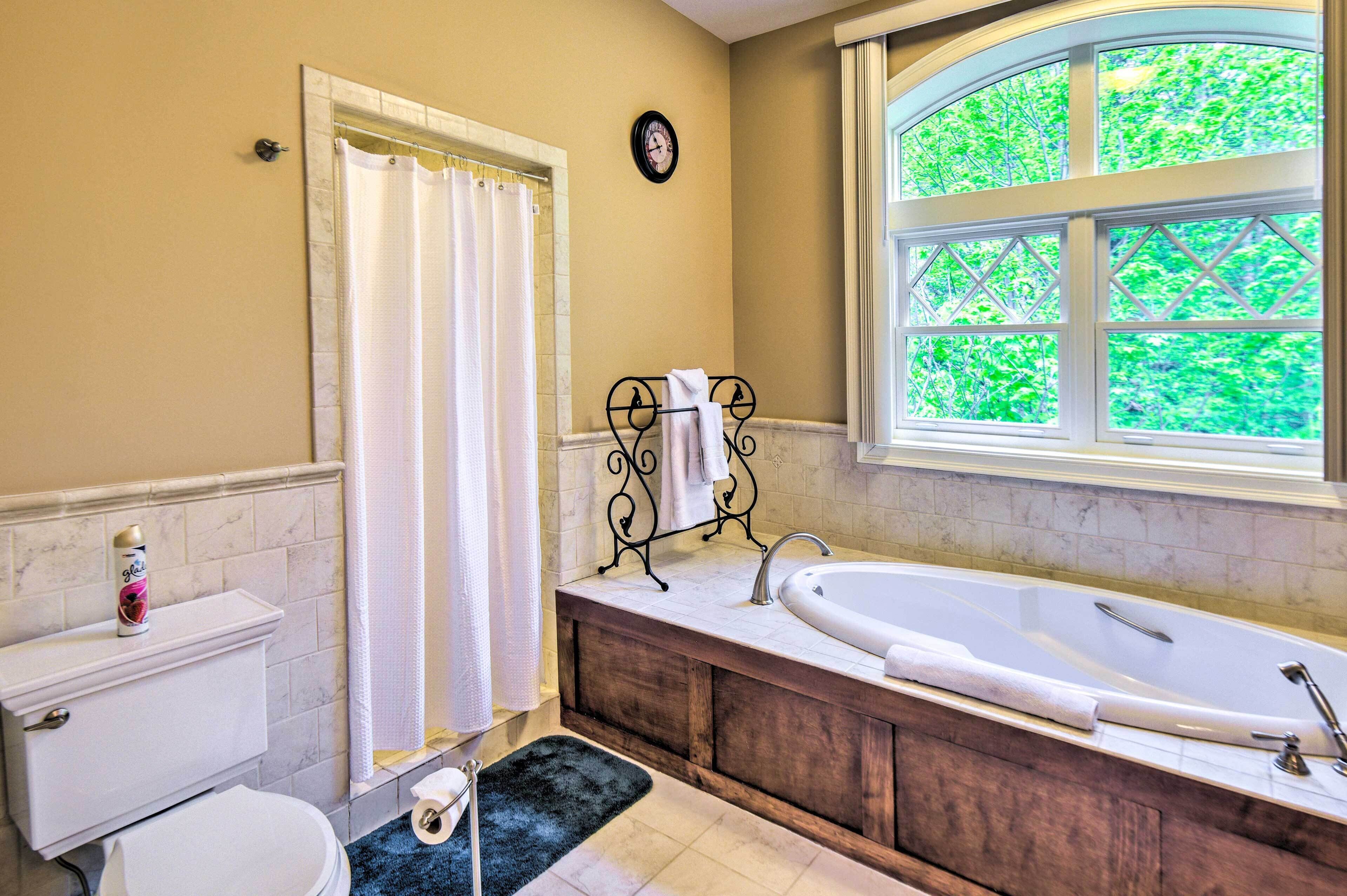 A bathroom with a bathtub, toilet, and a window with a view of greenery.