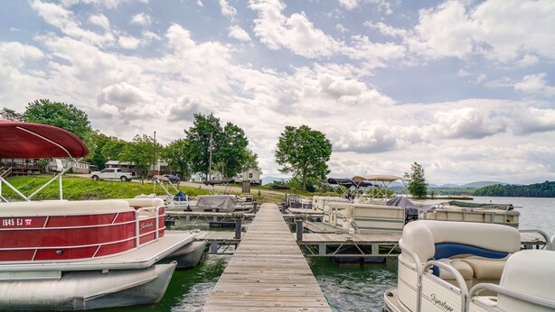 Un quai avec des bateaux, un espace abrité et une vue sur le lac et les collines.