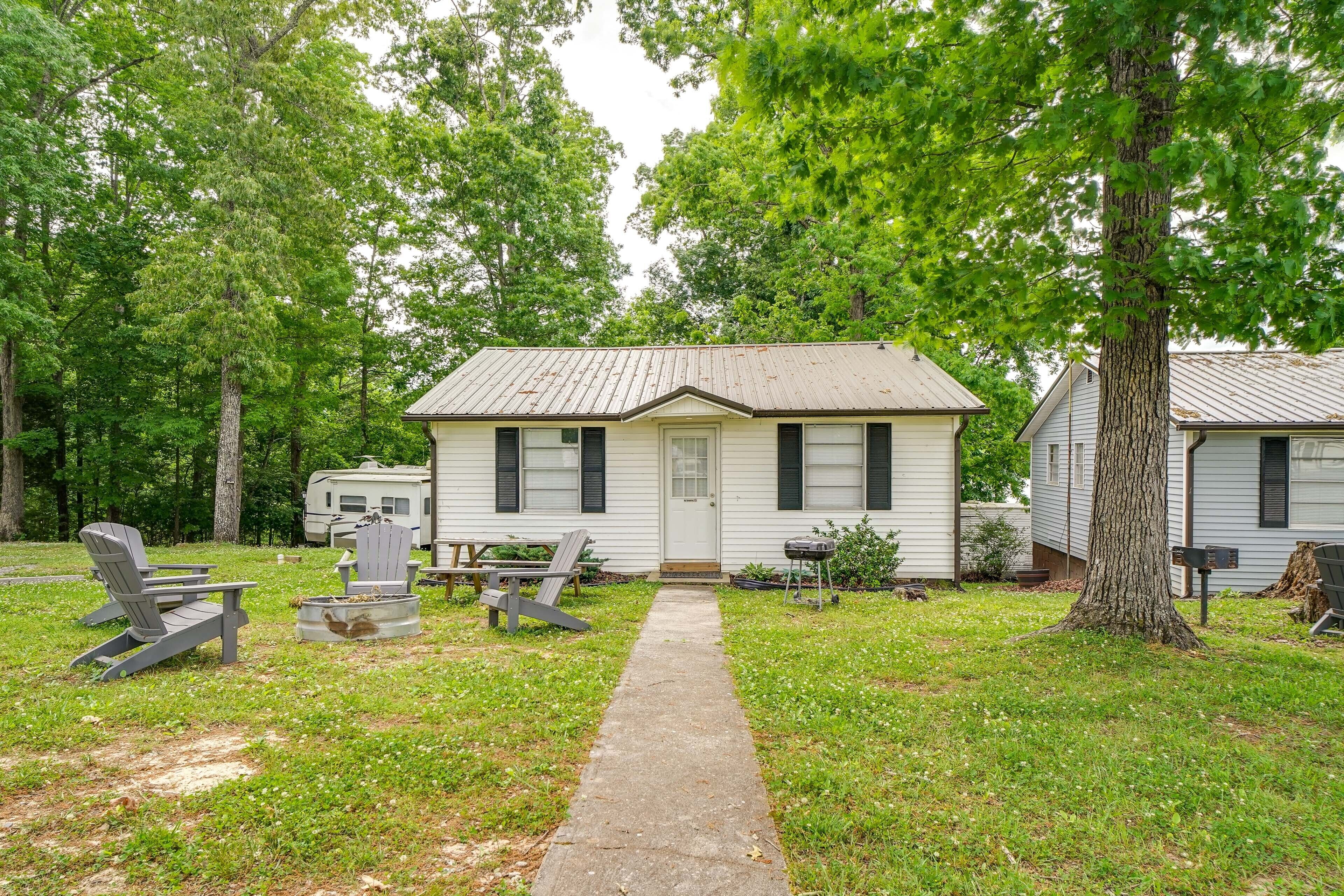 A small white house with a front porch, a pathway leading to the door, and two Adirondack chairs on the left.