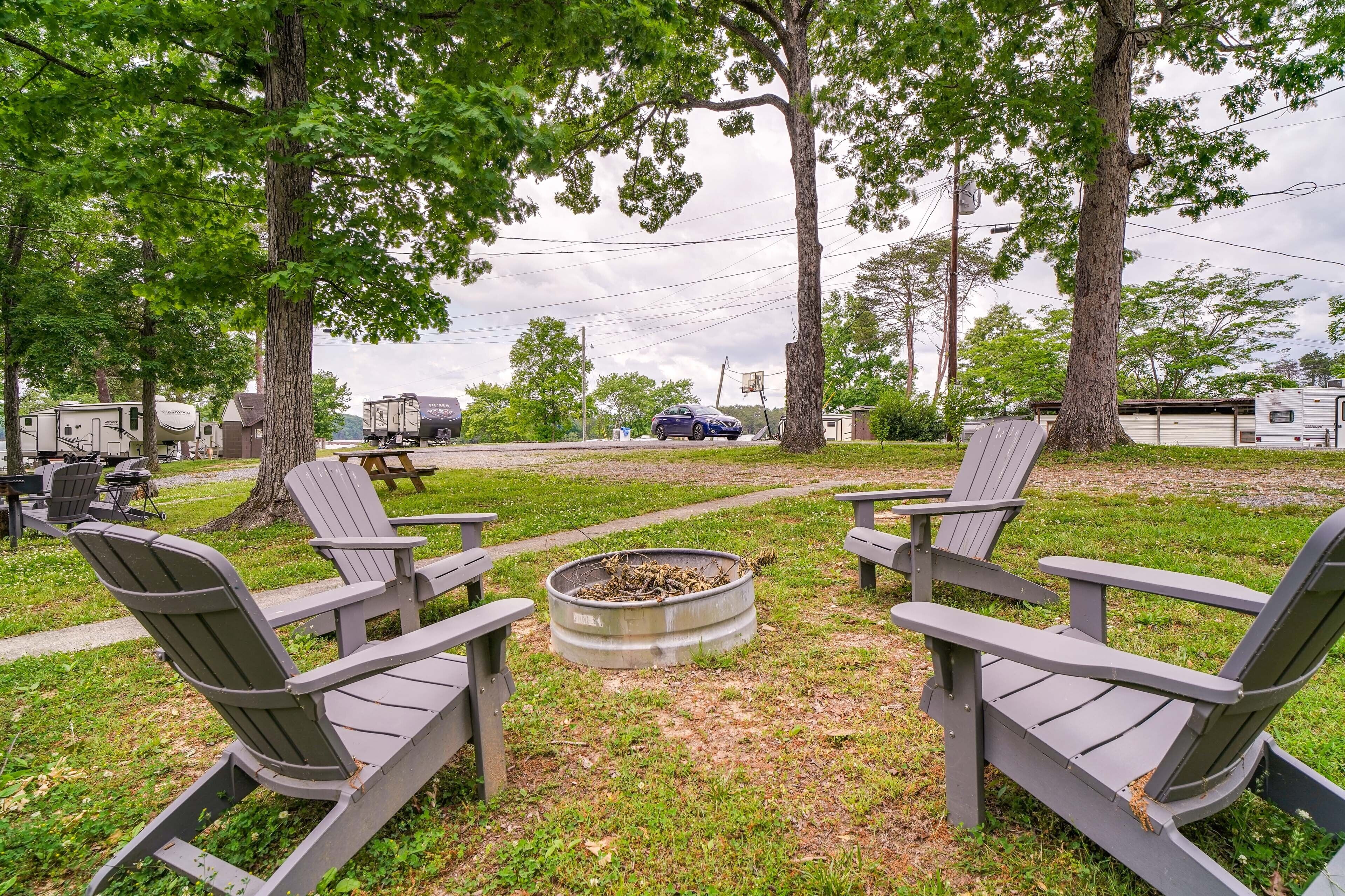 Un campamento con sillas Adirondack alrededor de un brasero, vehículos recreativos al fondo y una mesa de picnic.