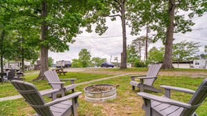 Un terrain de camping avec des chaises Adirondack disposées autour d’un foyer, des camping-cars en arrière-plan et une table de pique-nique.