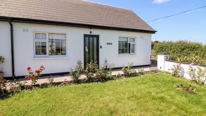 A single-story building with a white exterior, a dark roof, and a small garden area with various plants and flowers. - Cozy Cottage Retreat in Listowel pet Friend (Listowel)