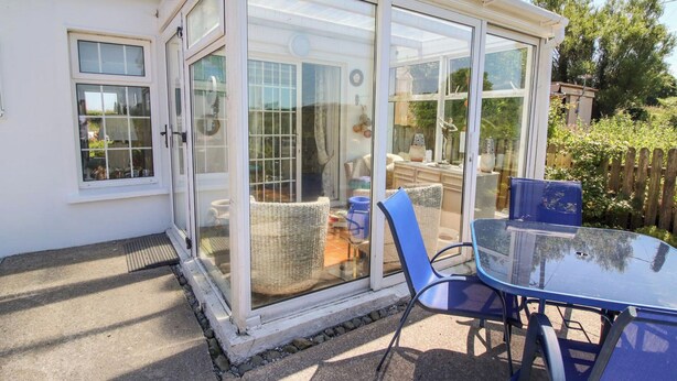 A conservatory with a glass door, wicker furniture, and a table with chairs. - Cozy Cottage Retreat in Listowel pet Friend (Listowel)