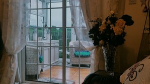 A room with a large window, a wicker sofa, a vase with flowers, and a wall-mounted star decoration. - Cozy Cottage Retreat in Listowel pet Friend (Listowel)