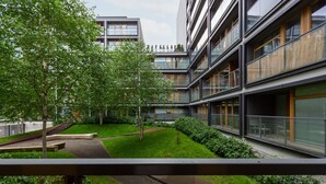 Un edificio moderno de varios pisos, con amplios ventanales y un patio con césped y árboles.