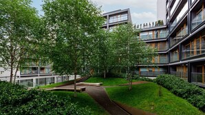 Un edificio moderno con un patio que incluye un camino, árboles y una pequeña fuente.