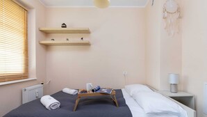 Una cama bien tendida con un edredón oscuro, una mesita de noche con una lámpara y una estantería con objetos decorativos.