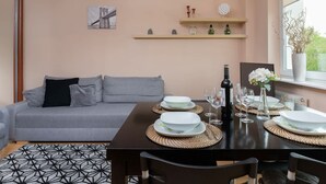 Un comedor con una mesa dispuesta para cuatro personas, un sofá gris y una estantería de pared con objetos decorativos.