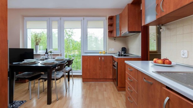 Cocina moderna con armarios de madera, comedor con mesa y sillas, y un ventanal que ofrece vistas al verdor.