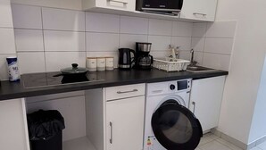 A compact kitchen with white cabinets, a microwave, a coffee maker, and a washing machine.