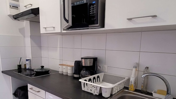 A modern kitchen with white cabinets, a built-in microwave, a coffee maker, a washing machine, and a sink.