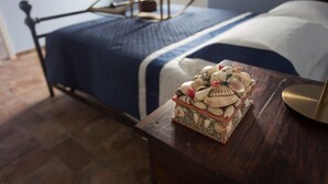 Un lit bien fait, recouvert d’une couvre-lit bleue et blanche, une table de chevet en bois ornée d’une composition décorative de coquillages et un cadre de lit en métal.