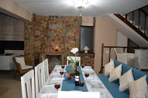 Un coin repas agrémenté d’un mur en pierre, d’une cheminée, d’une table à manger mise avec des assiettes, des verres et une bouteille de vin.