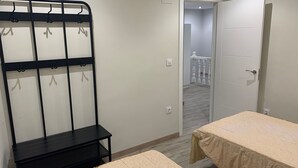 Quarto com duas camas, uma estante de metal preta, uma porta branca e vista para uma escadaria.