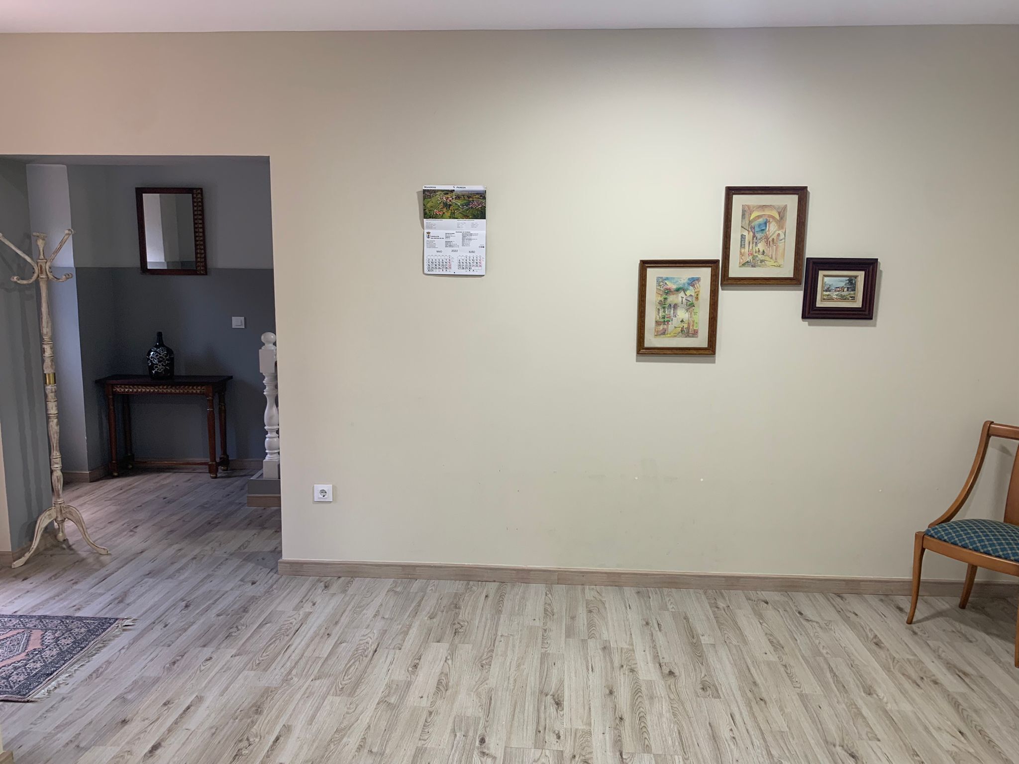 A room with a wooden floor, a chair, a table, and three framed pictures on the wall.