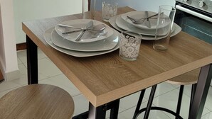 Un comedor con una mesa preparada para cuatro personas, un tragaluz arriba y una cocina al fondo.