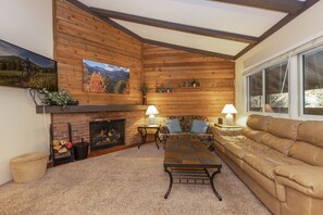Una sala de estar acogedora con chimenea, paredes de madera, un sofá de cuero y una mesa de centro.