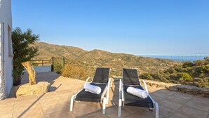 Two sun loungers on a patio with a view of a hilly landscape and the sea in the background. - Country house 15 minutes from the beach (Málaga)