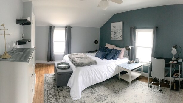 A bedroom with a bed, bedside table, desk, chair, and a ceiling fan.