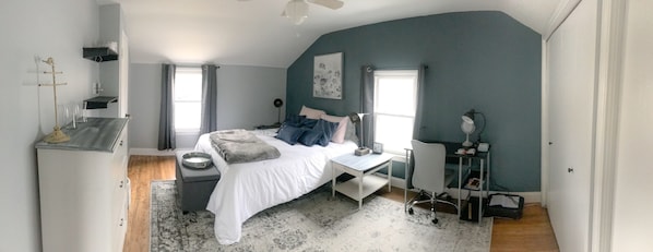 Quarto com cama, mesa de cabeceira, escrivaninha, cadeira e ventilador de teto.