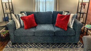 A grey sofa with red and white cushions, a patterned rug, and two floor lamps with a mesh design.