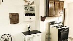 A compact kitchen with white cabinetry, a black countertop, a stove, and a chair.