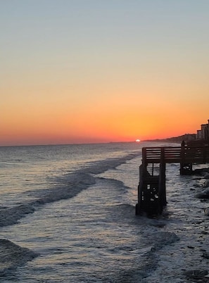 A sunset over the ocean with a wooden pier extending into the water.