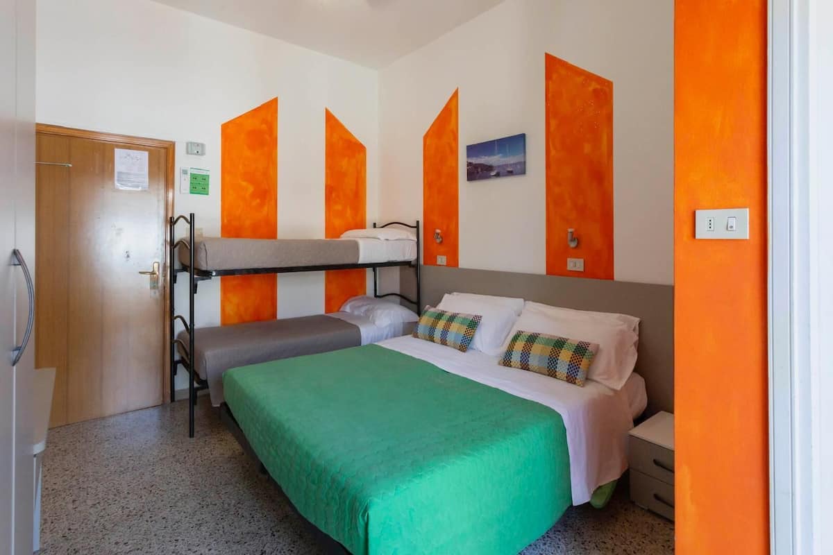 A single-bed room with a bunk bed against the wall, a green bedspread, and orange accent walls.