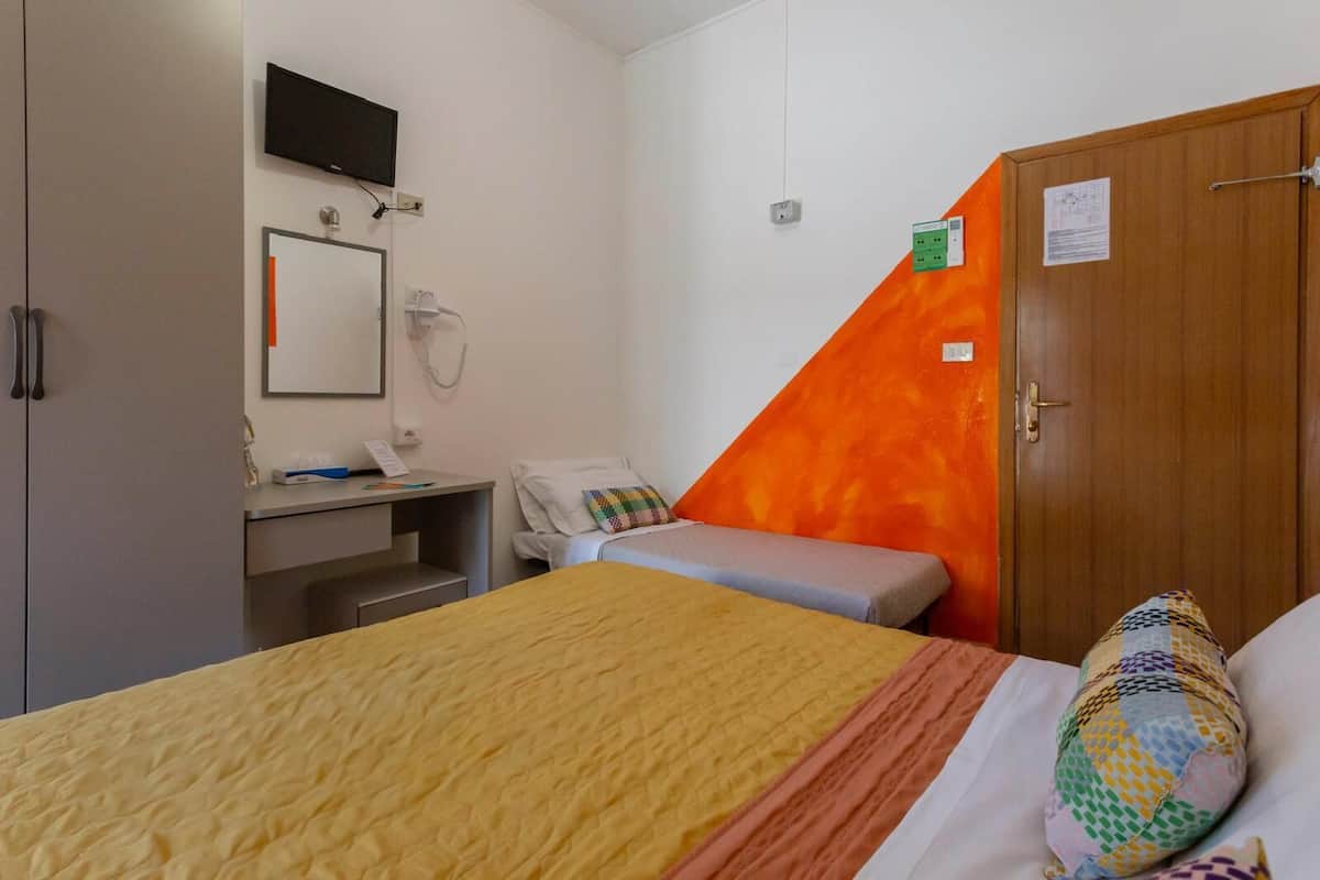 A bedroom with a bed, a desk, a chair, a wardrobe, and a television mounted on the wall.