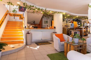 Un hall de hotel con escalera, mostrador de recepción, zona de estar y bar.