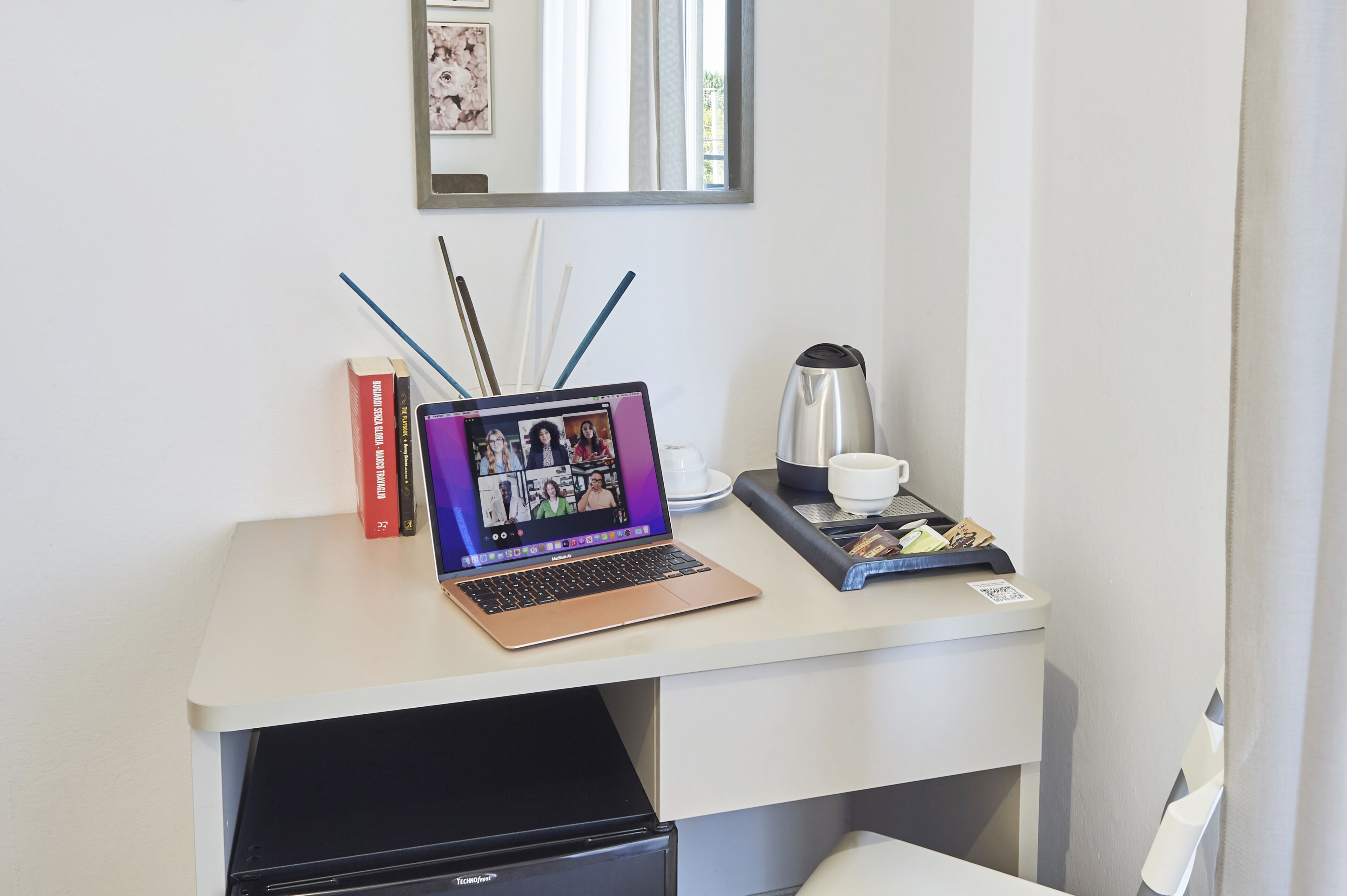 Un ordinateur portable sur un bureau, avec des livres, une machine à café et une tasse.