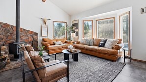 Ein geräumiges Wohnzimmer mit Kamin aus Stein, Ledersofas und großen Fenstern.