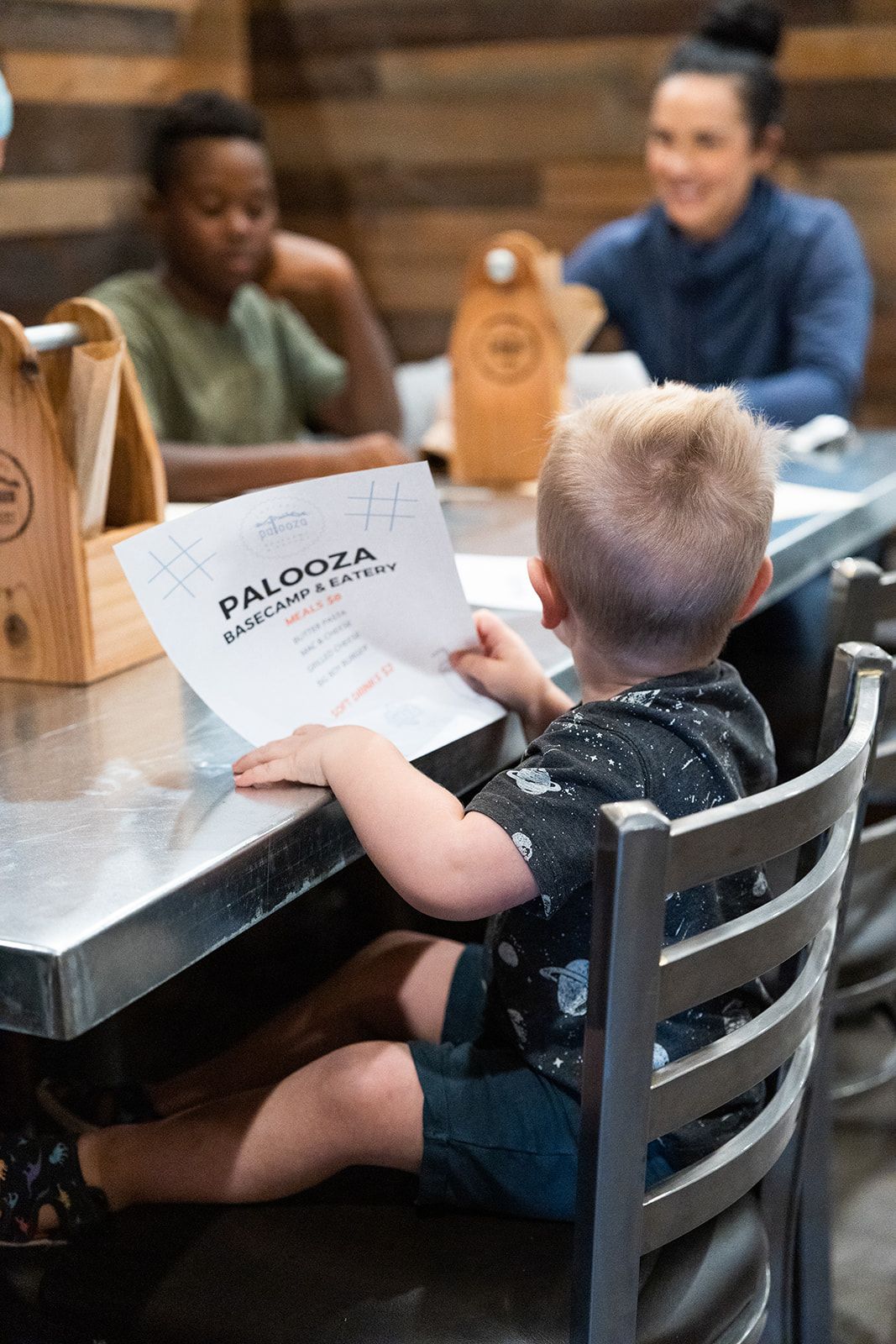 Criança sentada à mesa com um menu do Paloozza Basecamp & Eatery.