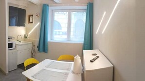 A compact room with a kitchenette, a small dining table, and a window with curtains.