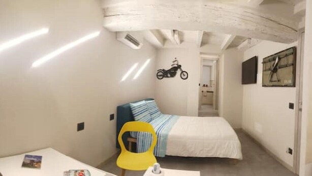 A compact room with a bed, a small desk, a chair, and a motorcycle symbol on the wall.