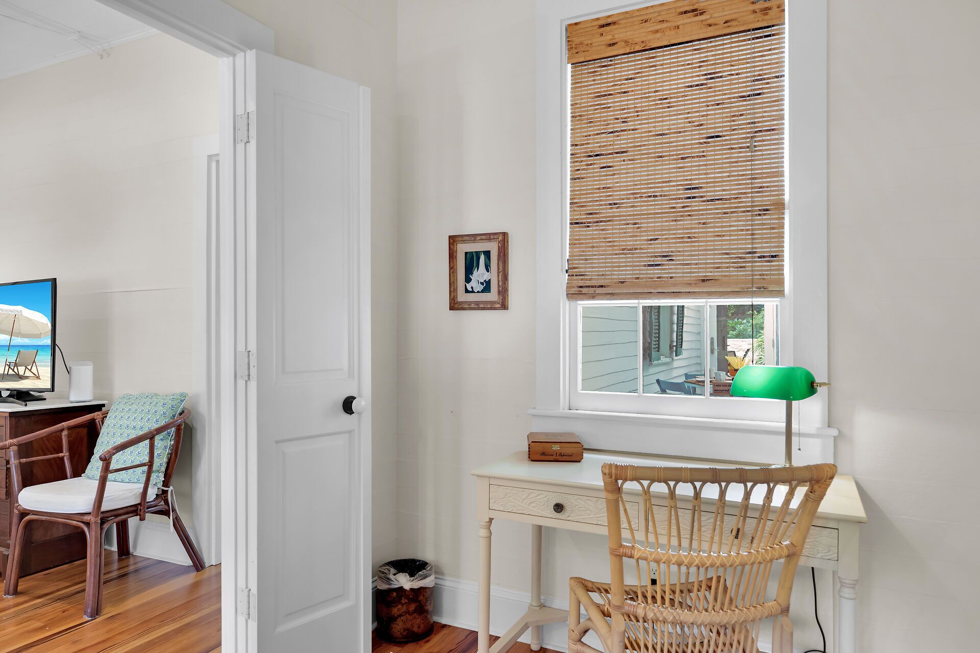 A room with a desk, a chair, a window with blinds, a picture frame, and a lamp.