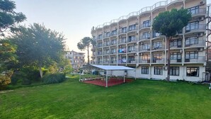 A multi-story residential building with balconies, a covered outdoor seating area, and a well-maintained lawn. - Orkide Otel (Didim)