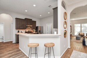 Une cuisine moderne avec des meubles de couleur sombre, un îlot central blanc doté de tabourets et une grande fenêtre.