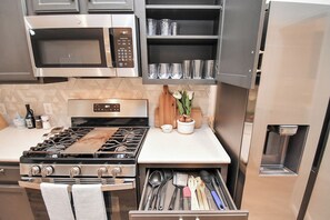 A modern kitchen with a gas stove, stainless steel appliances, and a built-in utensil drawer.