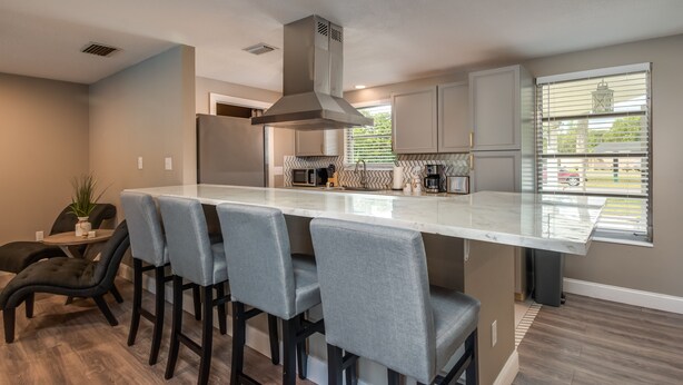 A modern kitchen with a central island, bar stools, and a view of the outside through a window. - ⭐️POOL|GAMEROOM*Lanai Hangout*Open Concept Design🌊 (Ocala)
