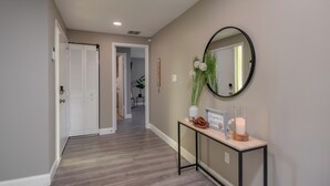 A hallway with a wooden floor, a white door, a console table with a mirror, and a welcome sign. - ⭐️POOL|GAMEROOM*Lanai Hangout*Open Concept Design🌊 (Ocala)