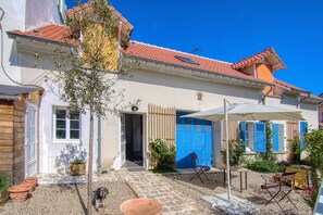 Uma casa com telhado de telhas, porta frontal e um pequeno jardim com mesa e cadeiras.