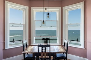 A dining area with a view of the ocean through large windows, a wooden table, and two chairs. - Stylish Beachfront Luxury With Sweeping Sea Views (Herne Bay)