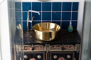 A bathroom with a gold basin, a faucet, and a soap dispenser on a dark countertop.