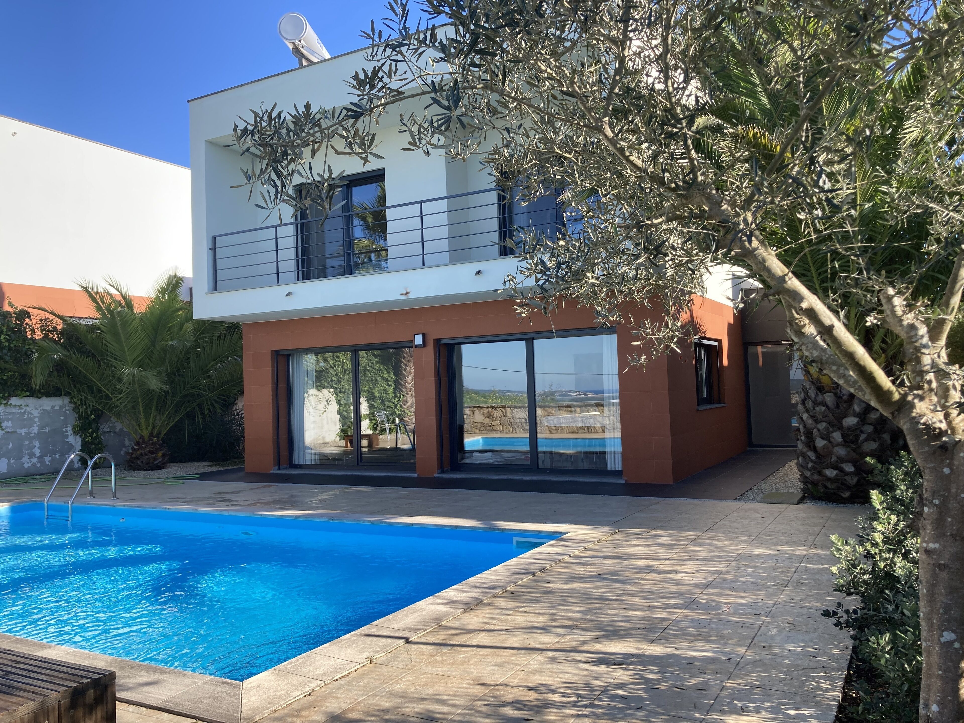 A modern two-story house with a swimming pool, large glass doors, and a balcony.