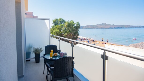 Un balcon avec une table et des chaises, donnant sur une plage animée et un ciel dégagé.