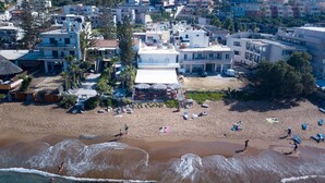 Un hôtel situé en bord de mer, doté de nombreuses chambres, d’une piscine et d’un espace plage aménagé avec des parasols et des chaises longues.