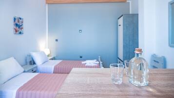 A hotel room with two beds, a wooden table with a bottle and glasses, and a painting on the wall.