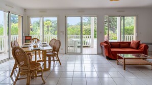 A spacious room with a dining area, a sofa, and a balcony with a view of greenery. - Swimming pool villa for 8 in Lacanau (Lacanau)