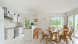A modern kitchen with white cabinets, a stainless steel dishwasher, and a dining area with a round table and wicker chairs. - Swimming pool villa for 8 in Lacanau (Lacanau)